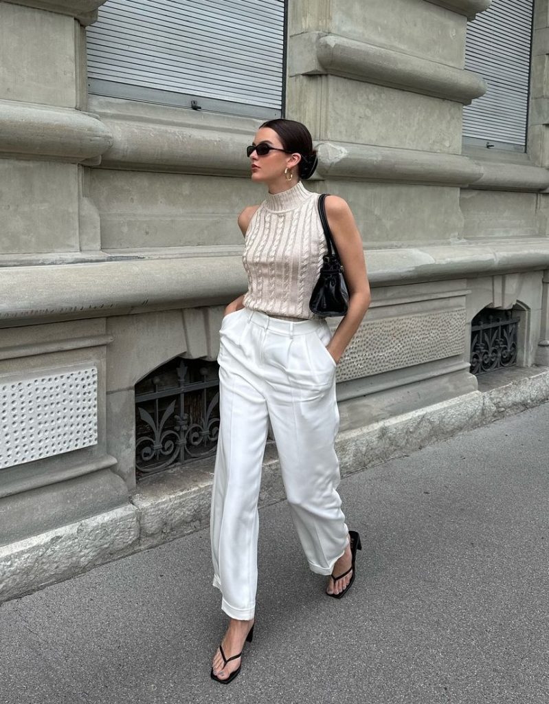 Mary usando óculos de sol, blusa de tricô gola alta off-white, calça de alfaiataria branca e chinelo kitten heels