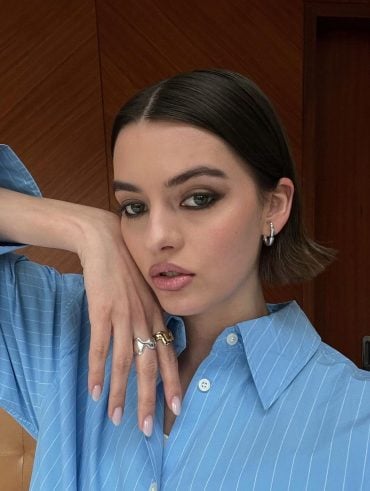 Mary usando camisa azul listrado, brinco cromado de argola média e anéis cromado e dourado