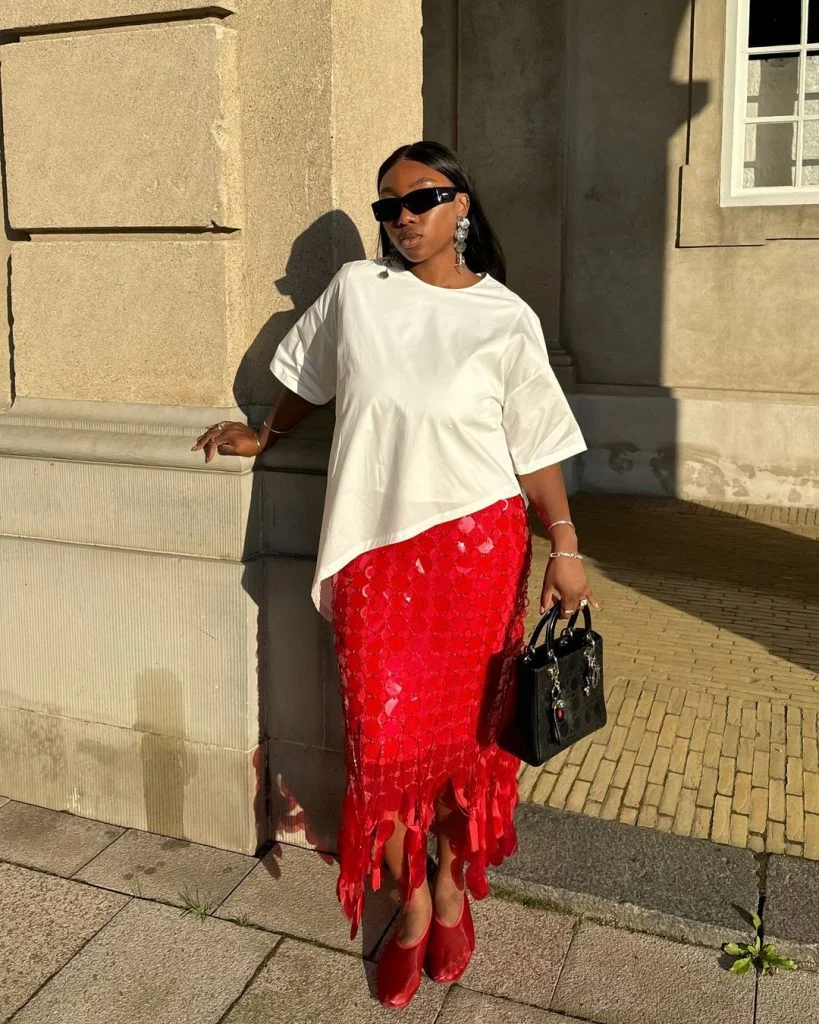 Nnenna usando óculos de sol, camiseta branca básica, saia vermelha midi glam e sapatilha mesh vermelha