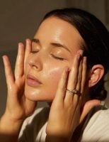 Mulher branca com cabelo preso e passando algum produto no rosto
