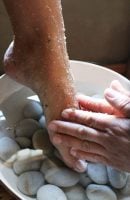 Pé branco com esfoliante sendo esfoliado por mãos brancas