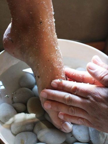 Pé branco com esfoliante sendo esfoliado por mãos brancas
