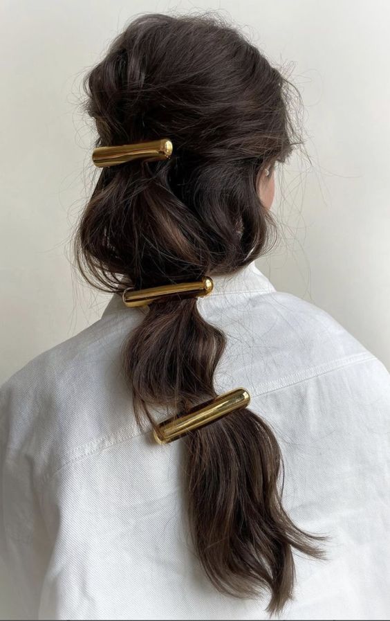 Mulher com cabelo longo escuro e presilhas maximalistas douradas