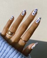 Mão branca com anéis dourados e unha amendoada com estampa azul
