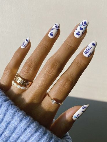 Mão branca com anéis dourados e unha amendoada com estampa azul