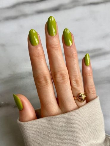 Mão branca com anel dourado e unha amendoada verde-folha