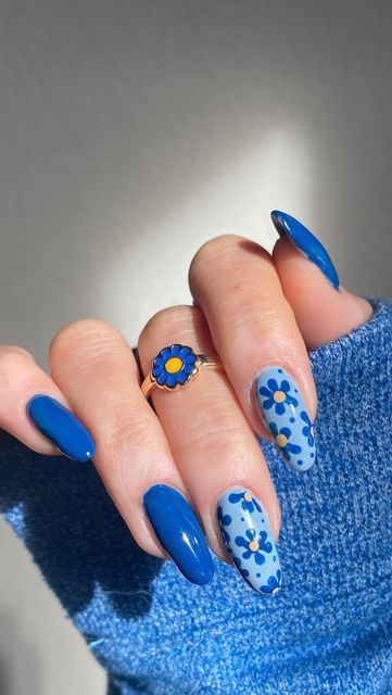 Mão branca curvada com anel de flor azul, unhas longas em azul e com decoração de flores