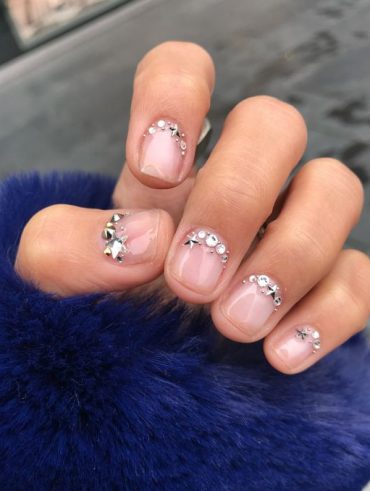 Mão branca meio fechada com unha curta decorada com francesinha invertida de strass