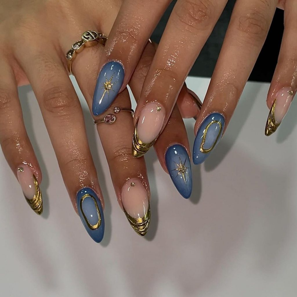 Mãos brancas com anéis dourados e unha stiletto azul-celeste com decorações em dourado 