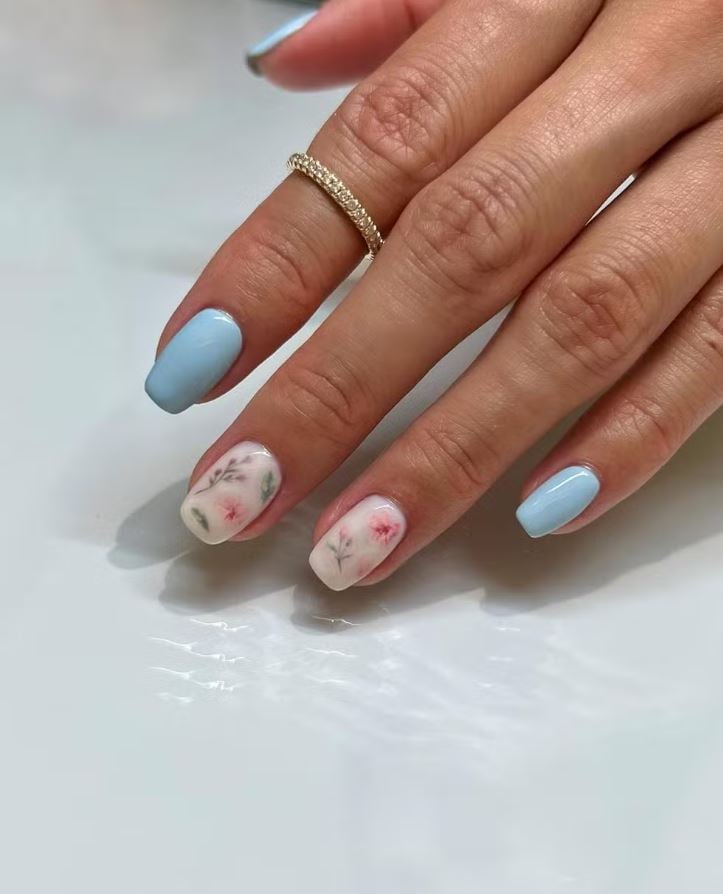 Mão branca com anel brilhante e unha quadrada azul-claro e branca com flores 