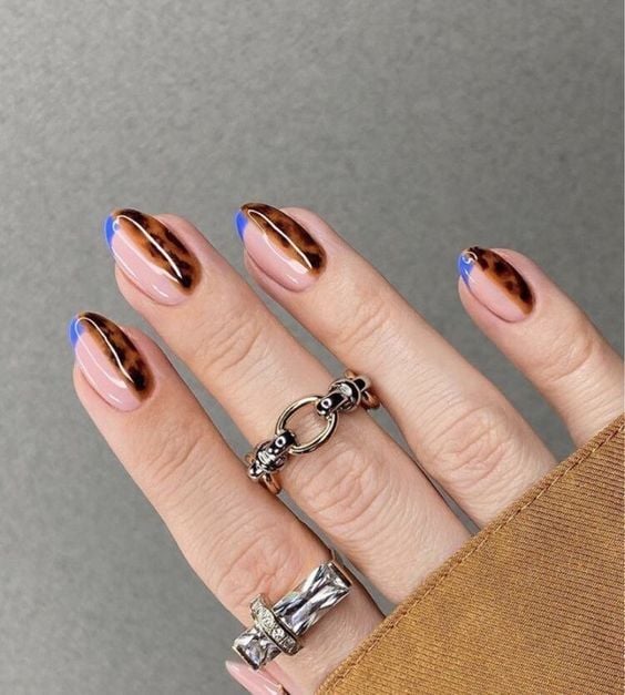 Mão branca com aneís e unha amendoada com francesinha azul e metade com estampa de tartaruga