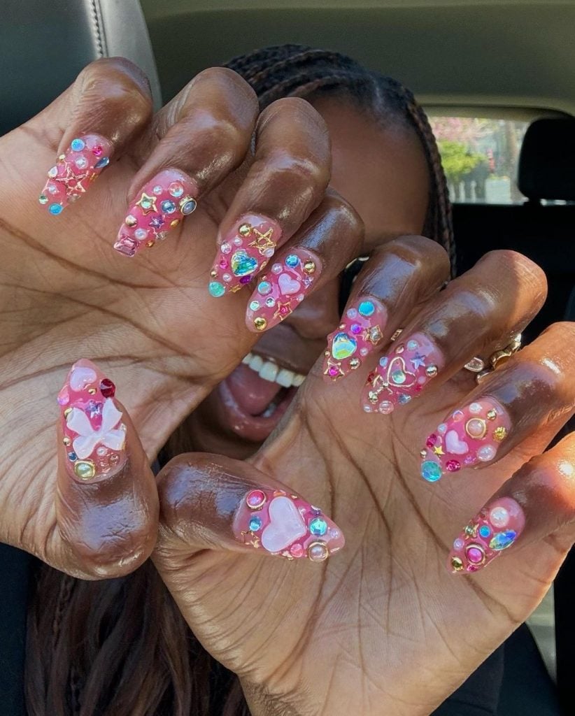 Mãos negras curvadas com unha arredondada rosa com aplicações