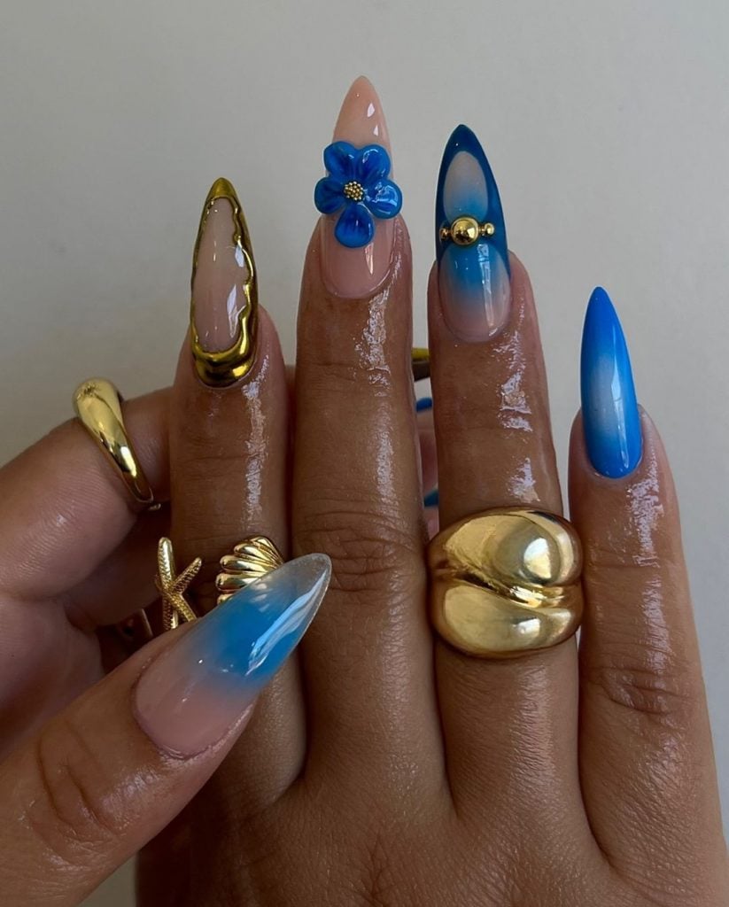 Mãos negras com anéis dourados e unha stiletto azul maximalista