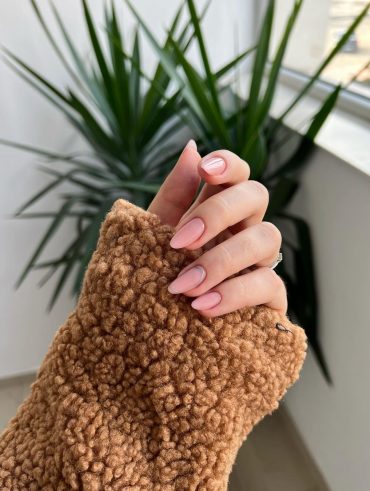 Mão branca curvada com unha amendoada média nude rosada com decoração metálica