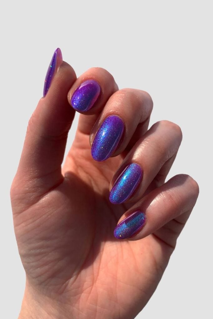 Mão curvada com unha roxa holográfica