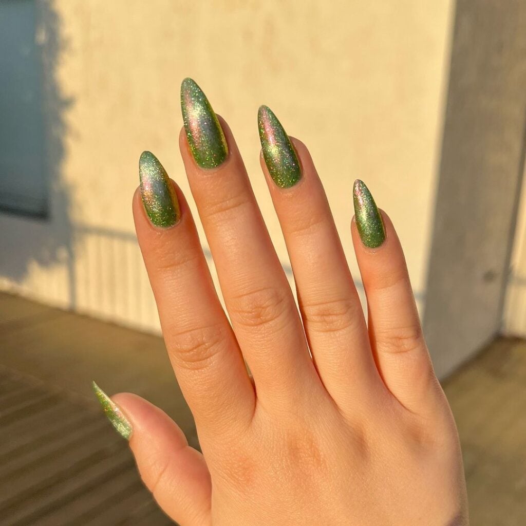 Mão branca com unha holográfica verde e formato stiletto