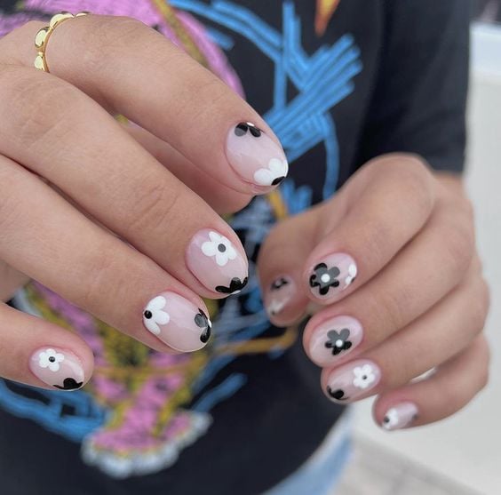 Mãos brancas com unhas curtas arredondadas com flores brancas e pretas 