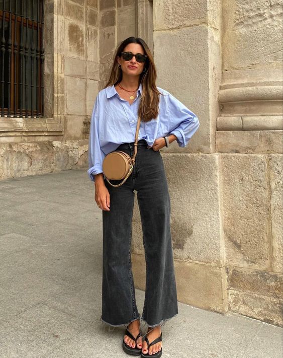 Mulher jovem e magra de pele clara. Ela veste camisa azul e calça cinza com chinelo preto.