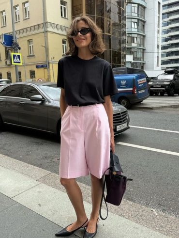 Mulher jovem, magra e de pele clara com cabelo médio e loiro. Ela veste camiseta, bermuda com cinto e slingback.