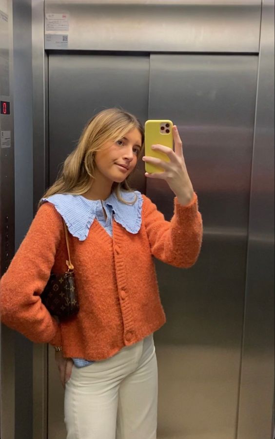 Mulher jovem de pele clara. Ela veste cardigan laranja. 