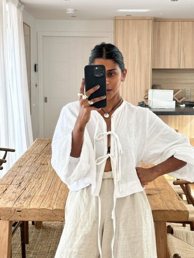 Mulher jovem e negra, tirando foto no espelho, com cabelo preso em coque, usando blusa boho com abertura em amarrações na parte frontal.