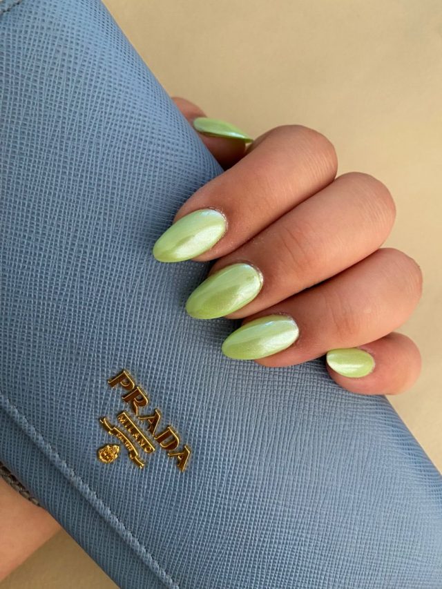 Mão segurando uma bolsa da Prada em tonalidade azul-claro e unhas pintadas de verde-claro