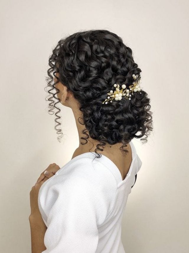 Mulher, noiva, com cabelo cacheado em penteado de coque com acessório de flor