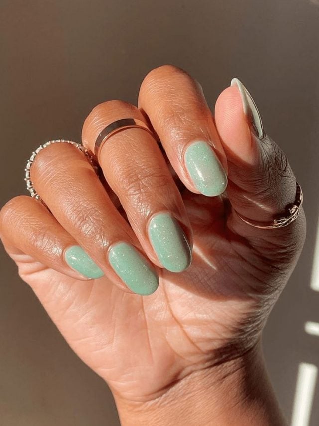 Mão branca curvada com anel e unha amendoada verde-menta brilhosa