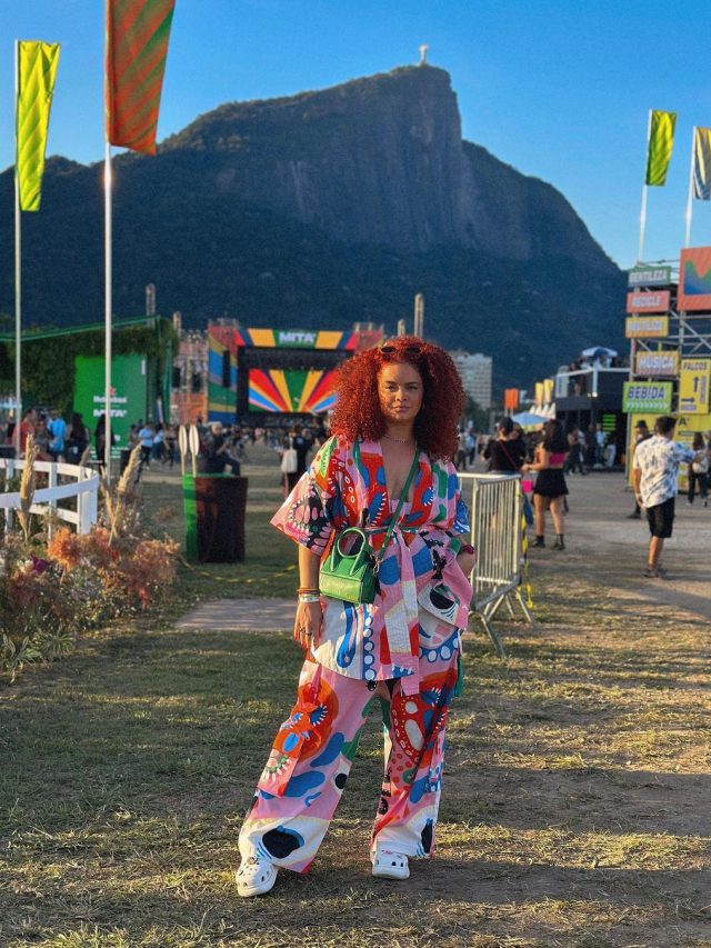 Mulher jovem de pele escura. Ela usa look colorido em festival.