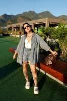Mulher jovem de pele clara e magra. Ela usa bermuda jeans e camiseta e calçado branco (Crocs)