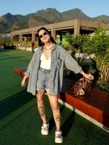 Mulher jovem de pele clara e magra. Ela usa bermuda jeans e camiseta e calçado branco (Crocs)