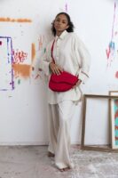 Mulher jovem e negra usando look neutro, com camisa, calça e uma bolsa vermelha