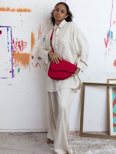 Mulher jovem e negra usando look neutro, com camisa, calça e uma bolsa vermelha