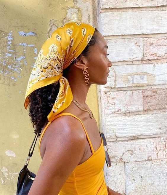 Mulher negra e jovem, usando lenço de cabelo na tonalidade amarela