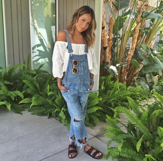Mulher jovem, magra e branca, usando blusa ciganinha, jardineira jeans e usando papete.