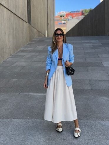 Mulher branca, com cabelo médio em cor castanho claro, usando óculos de sol, blazer azul, saia branca e slingback.