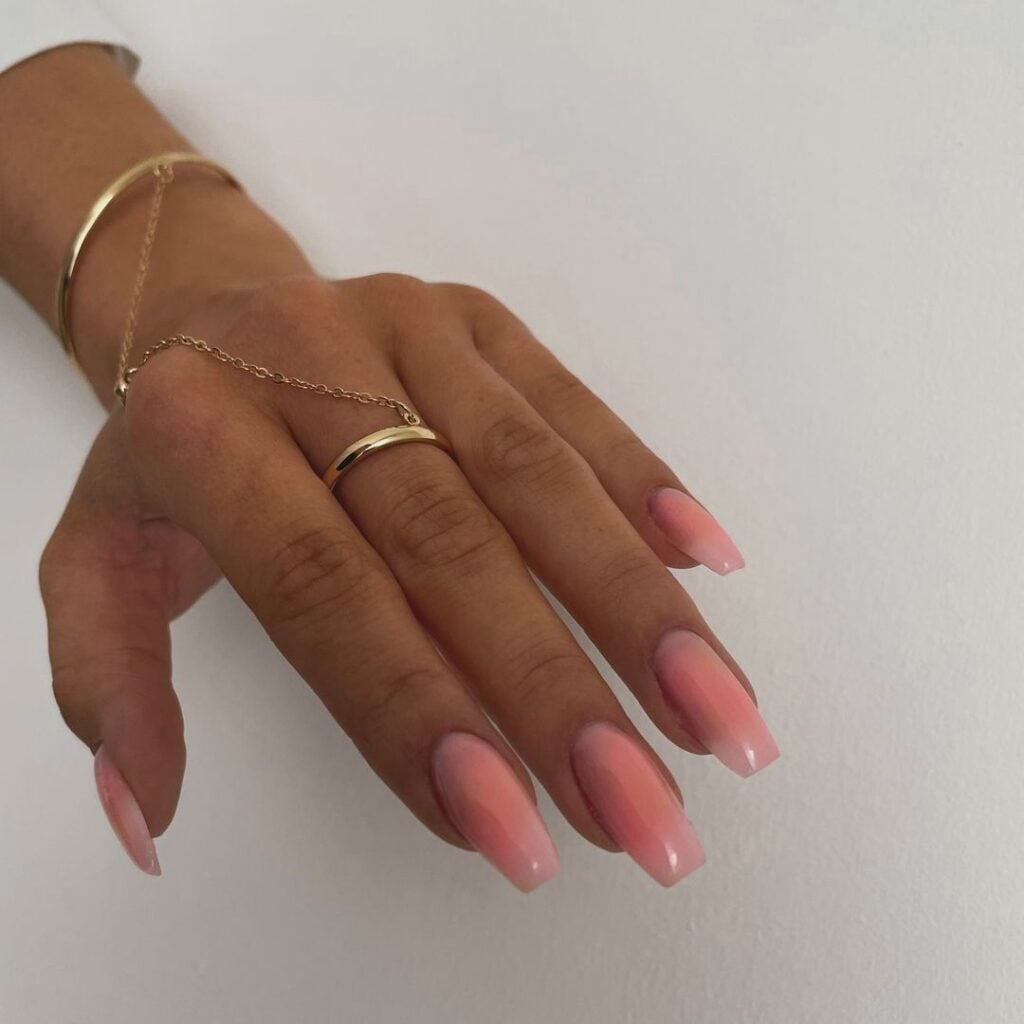 Mão de pele branca, com anel dourado e unha bailarina rosa brush