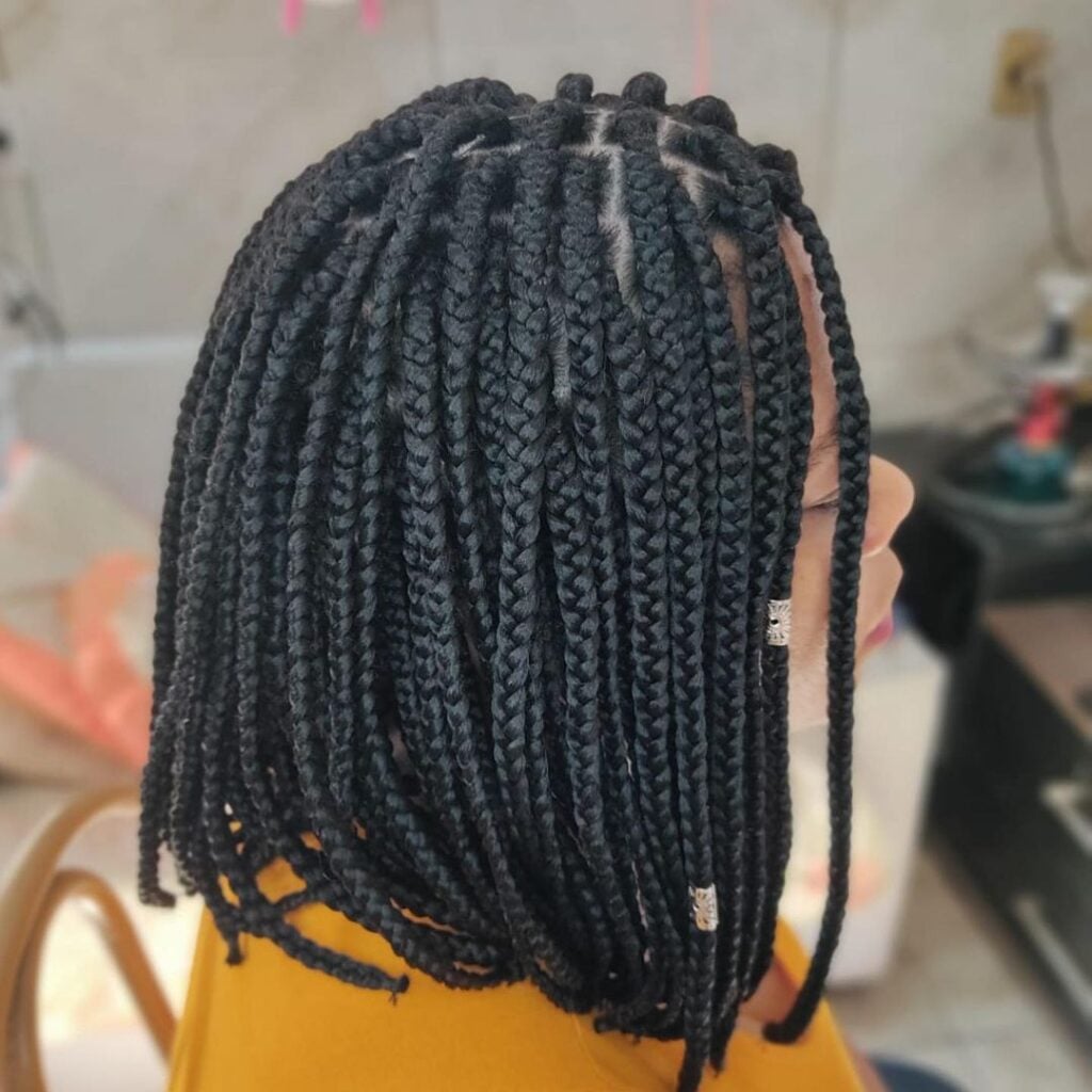 Mulher negra, com cabelo preto e com trança, com corte curto e chanel