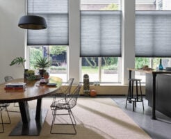 Espaço com mesa oval de madeira, cadeiras de metal e cortinas