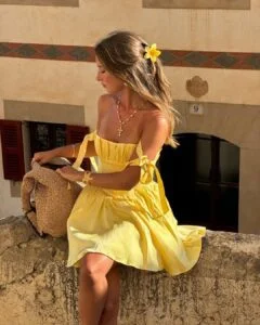 Kezia Rose Cook com acessório de flor no cabelo, vestido amarelo-manteiga e maxi bag