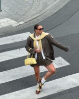 Lara com bolsa amarelo-manteiga, suéter amarelo-manteiga, blazer oversized, minissaia plissada de alfaiataria e tênis Adidas SL 72