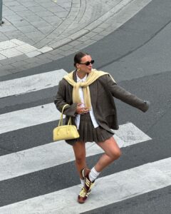 Lara com bolsa amarelo-manteiga, suéter amarelo-manteiga, blazer oversized, minissaia plissada de alfaiataria e tênis Adidas SL 72