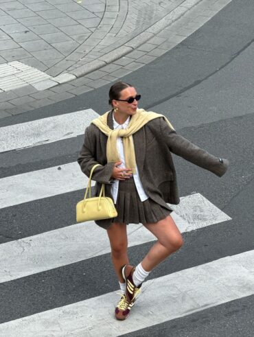 Lara com bolsa amarelo-manteiga, suéter amarelo-manteiga, blazer oversized, minissaia plissada de alfaiataria e tênis Adidas SL 72