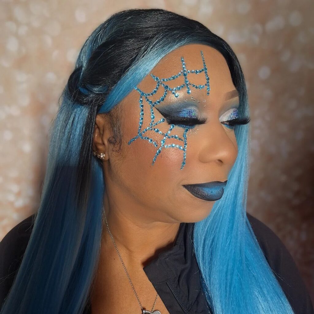 Mulher de pele preta, com peruca preta e azul e maquiagem com strass azul