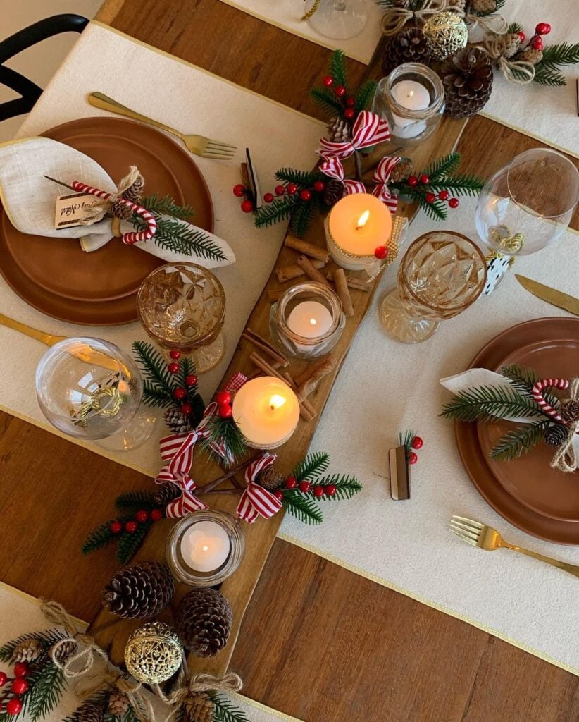 Mesa posta de Natal, com guardanapo decorado e centro de mesa com velas, canela, pinhas e plantas
