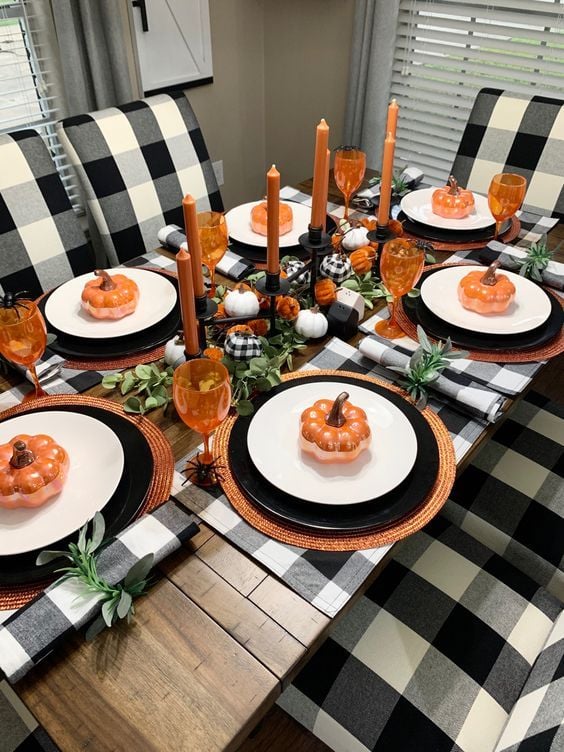 Mesa de madeira decorada com jogos americanos, louças brancas e pretas e abóboras