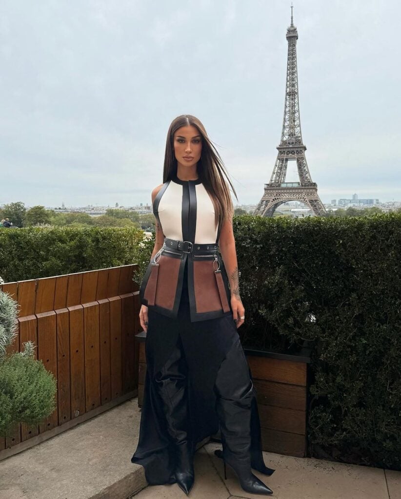 Bianca Andrade em Paris usando colete de couro com detalhes em fivela, saia preta com aberturas e bota preta de cano alto.