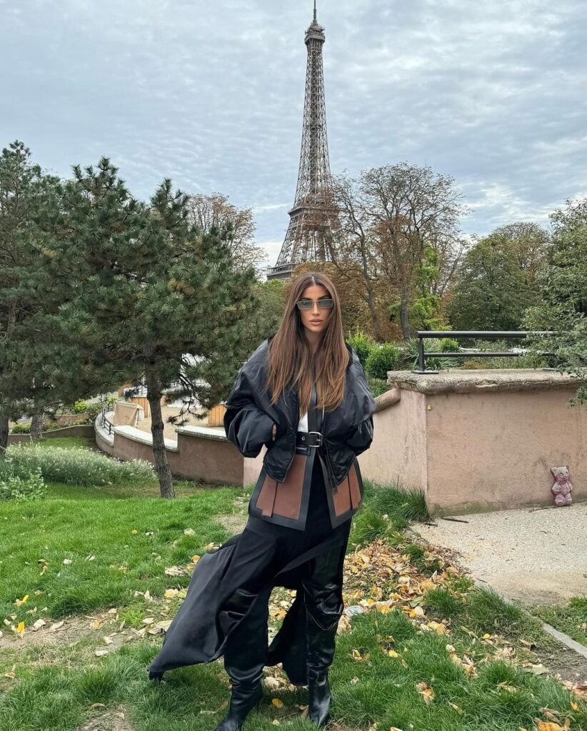 Bianca Andrade em Paris, usando jaqueta preta, saia com aberturas e botas de cano alto na cor preta.