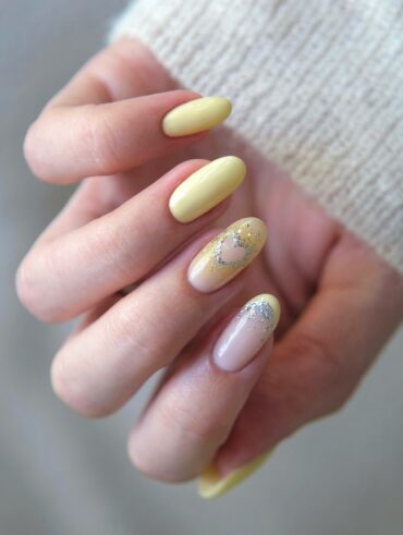 Mão de pele branca com unha amendoada amarelo-manteiga com decorações em azul