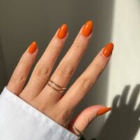 Mão de pele branca com anéis e unha amendoada laranja-queimado